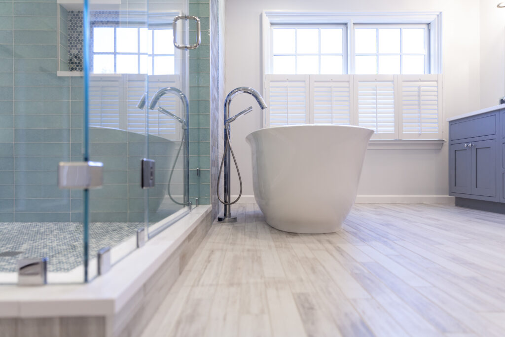 Bright bathroom remodel with a frameless glass shower, soft blue wall tile, freestanding soaking tub, and light wood-look flooring