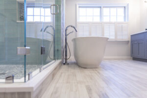Bright bathroom remodel with a frameless glass shower, soft blue wall tile, freestanding soaking tub, and light wood-look flooring