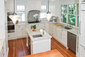 Custom kitchen renovation featuring white cabinets, marble countertops, island sink, and modern lighting